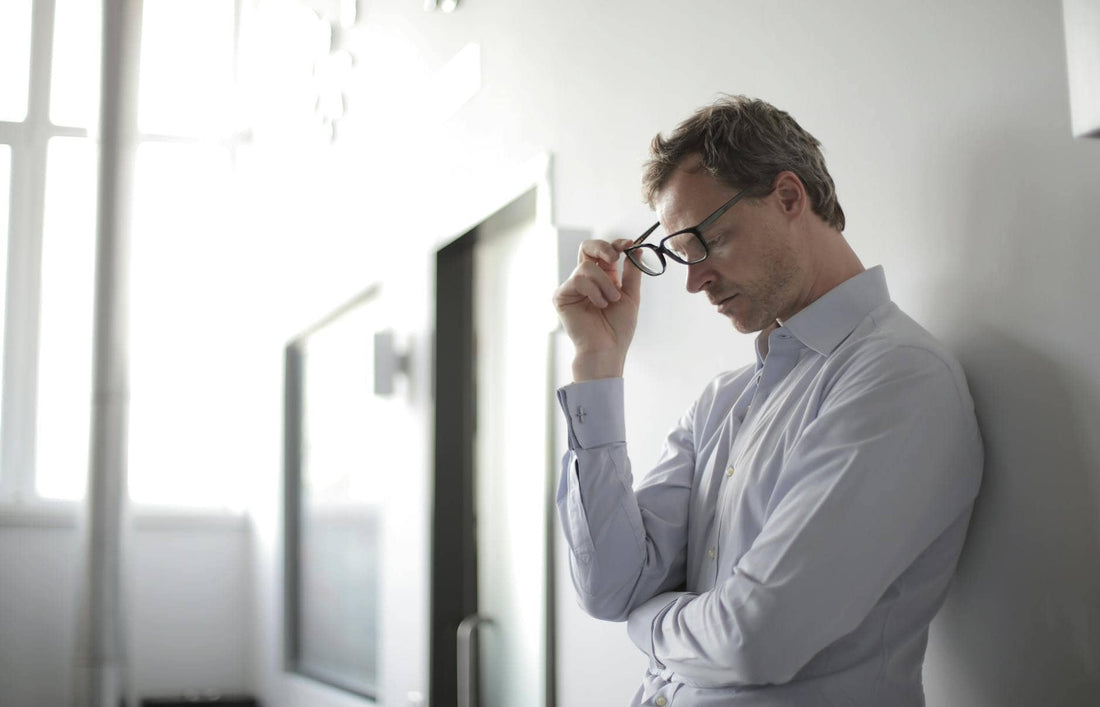 A professional pausing at his desk holding his glasses, looking drained